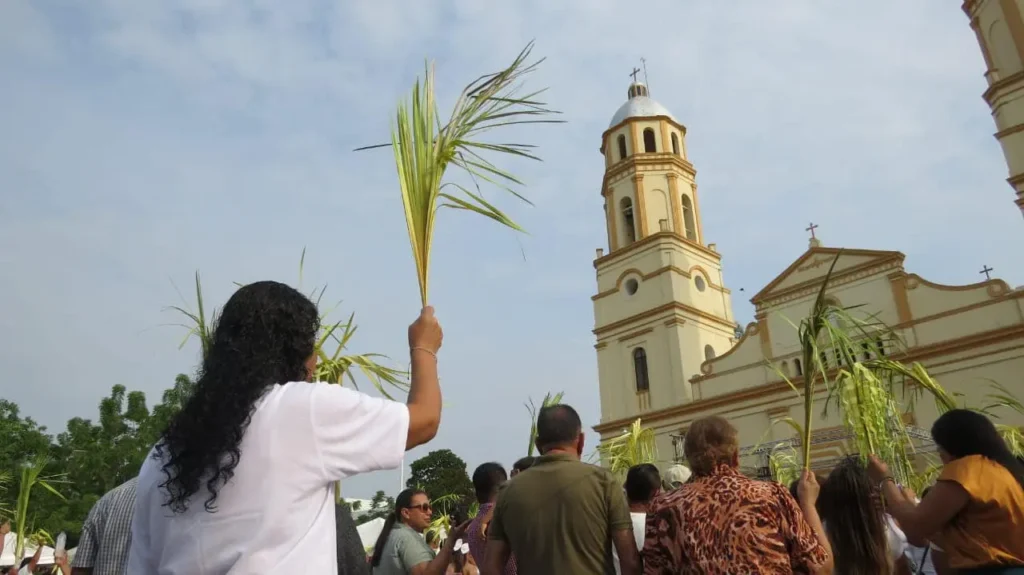 Persona sosteniendo un ramo de palma y de fondo la Iglesia San Antonio de Padua